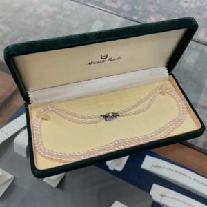 Green velvet jewelry box opened to reveal a double-strand Mikimoto pearl necklace with a decorative clasp.