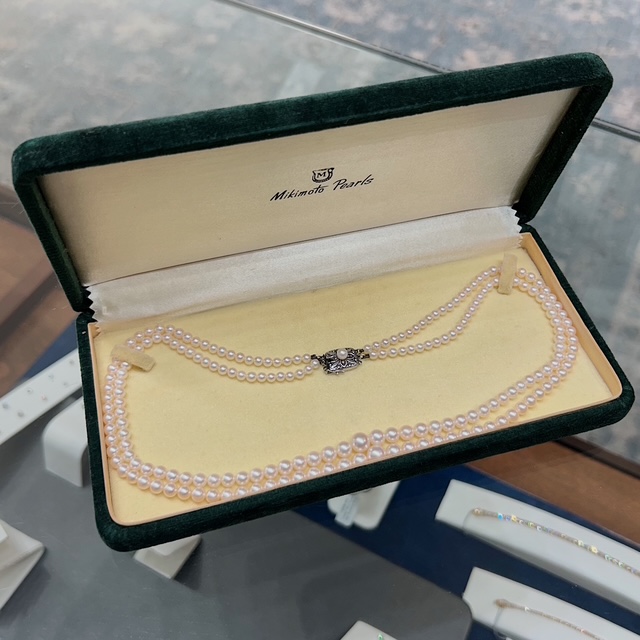 Green velvet jewelry box opened to reveal a double-strand Mikimoto pearl necklace with a decorative clasp.