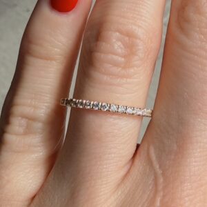 Slim rose-gold diamond eternity ring on a finger with red nail polish from a close-up perspective.