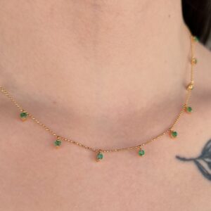 Delicate gold chain necklace with multiple small green stones around the neck.