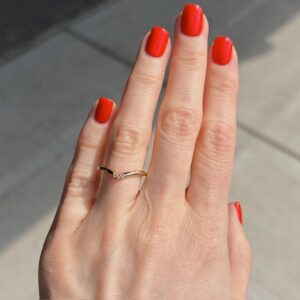 Close-up of a hand with bright red nails and a thin gold ring on the ring finger.