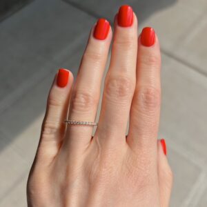 Close-up of a hand with bright red nails wearing a thin diamond eternity ring on the ring finger