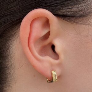 Close-up of a human ear wearing a small gold rectangular hoop earring on the earlobe