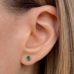 Close-up of a female ear with a green emerald stud earring in the earlobe crust area.