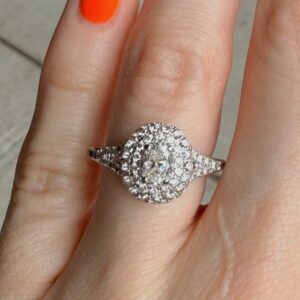 Engagement-style ring with a round center diamond surrounded by a halo of pavé diamonds on a finger with orange nail polish