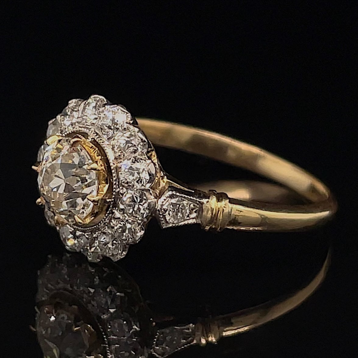 Gold halo engagement ring with a central diamond surrounded by smaller diamonds on a black background.