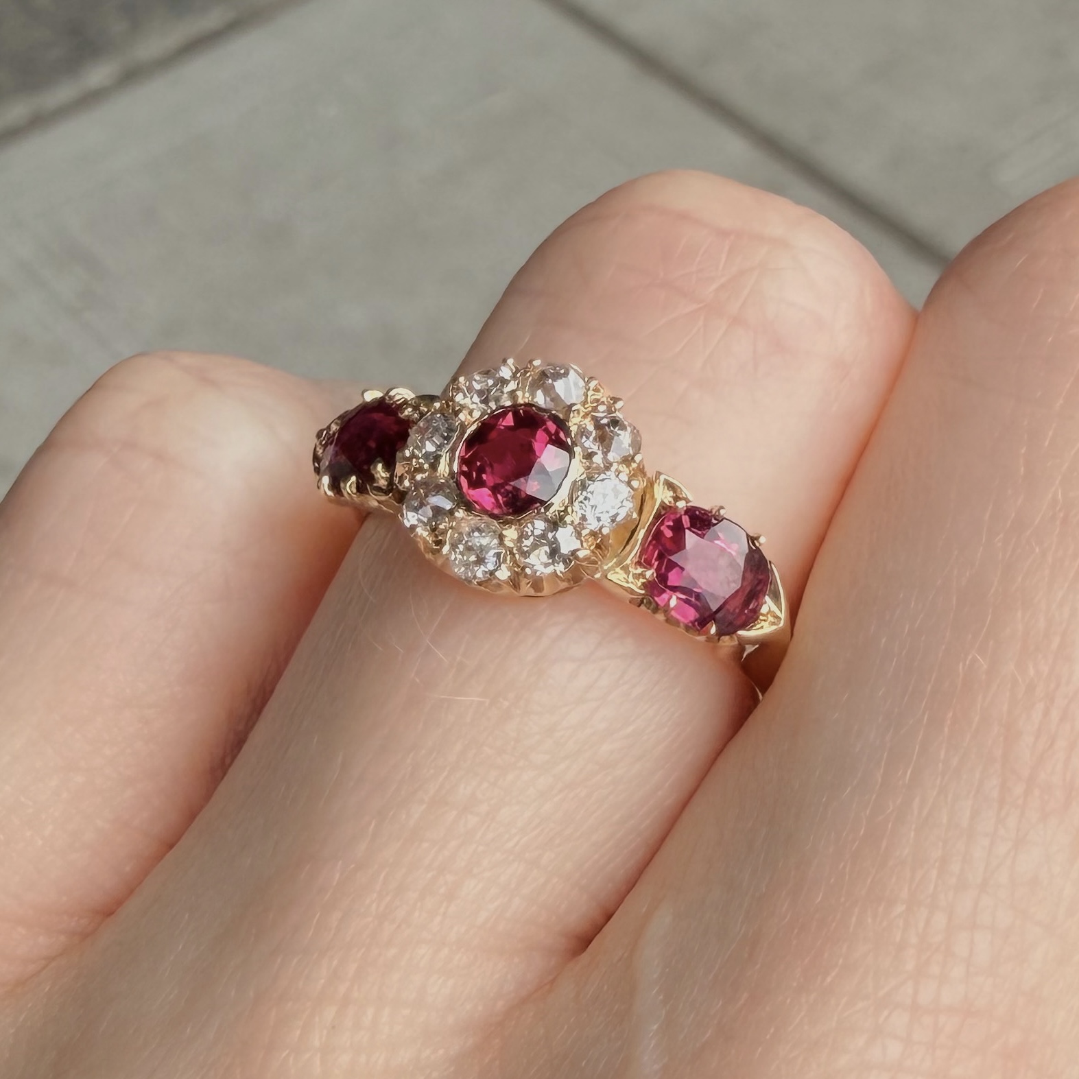 Gold ring with large red gemstone and surrounding diamonds on a finger.