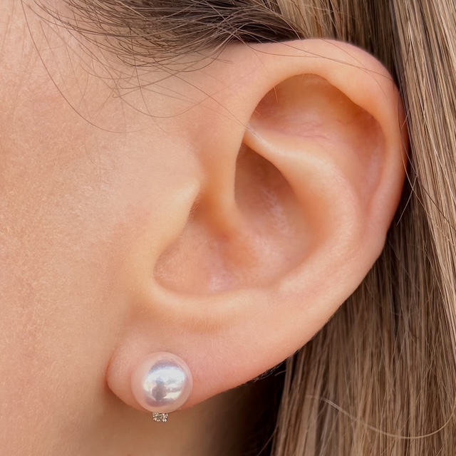 Close-up of a woman's ear wearing a pearl stud earring with a tiny diamond beneath it.