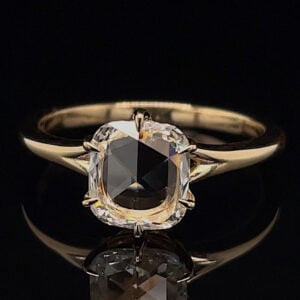 Gold solitaire ring featuring a cushion-cut diamond held by four prongs against a black background.