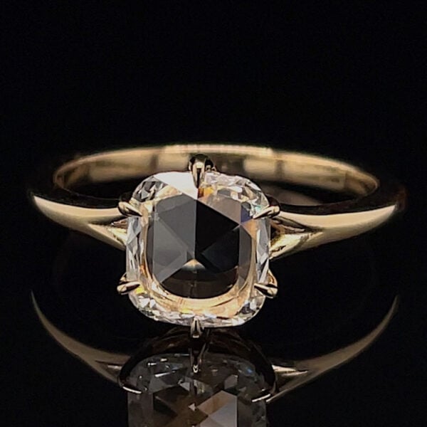Gold solitaire ring featuring a cushion-cut diamond held by four prongs against a black background.