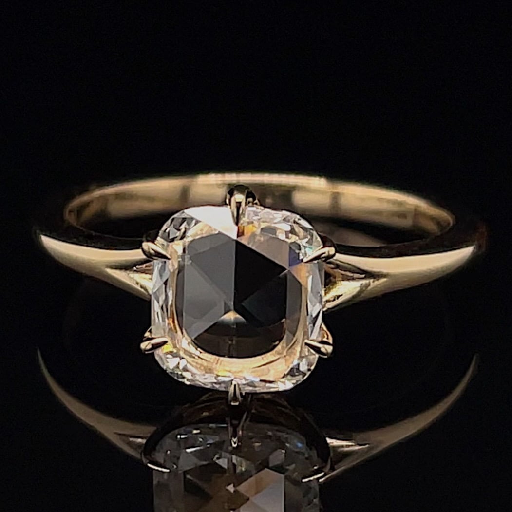 Gold solitaire ring featuring a cushion-cut diamond held by four prongs against a black background.