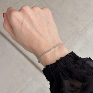 Delicate diamond tennis bracelet on a woman's wrist with a black, sheer sleeve edge visible.