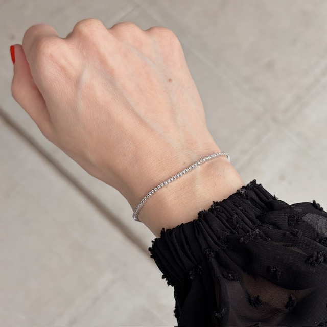 Delicate diamond tennis bracelet on a woman's wrist with a black, sheer sleeve edge visible.