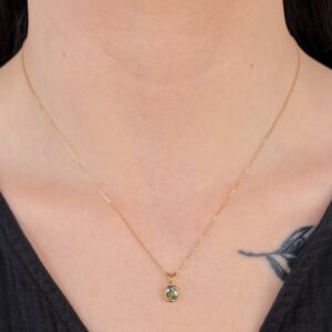 Gold necklace with a small oval gemstone pendant resting on the collarbone, tattoo peeking from the shoulder edge.