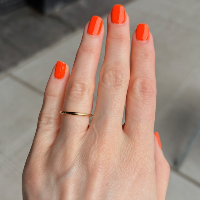 Close-up of a hand with bright orange nails and a thin gold ring on the ring finger.