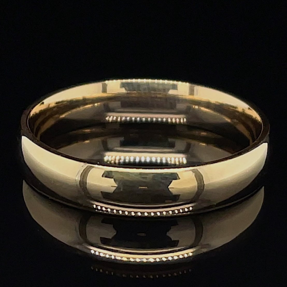 Close-up of a polished gold ring with an interlocking pattern around the band, set against a black background.