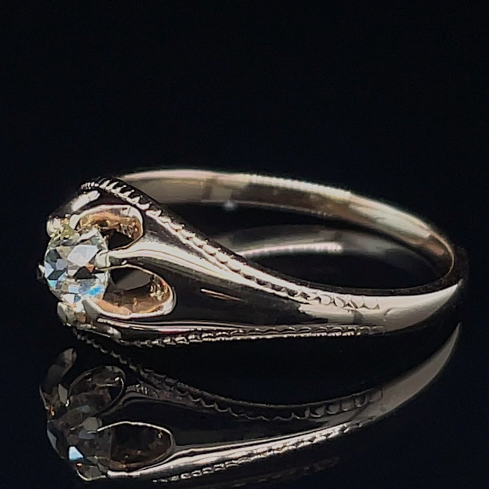 Diamond solitaire engagement ring with a round gem and braided/milled shoulders on a black reflective surface.
