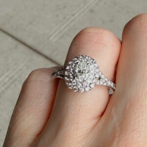 Diamond halo engagement ring on a finger, center stone surrounded by smaller diamonds on a pavé band.