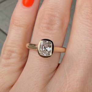Rose gold ring with a cushion-cut diamond on a finger, shown in close-up.