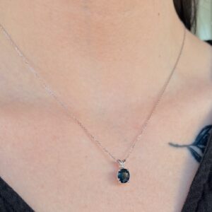Silver chain necklace with an oval dark-blue gemstone pendant resting on the wearer's collarbone.