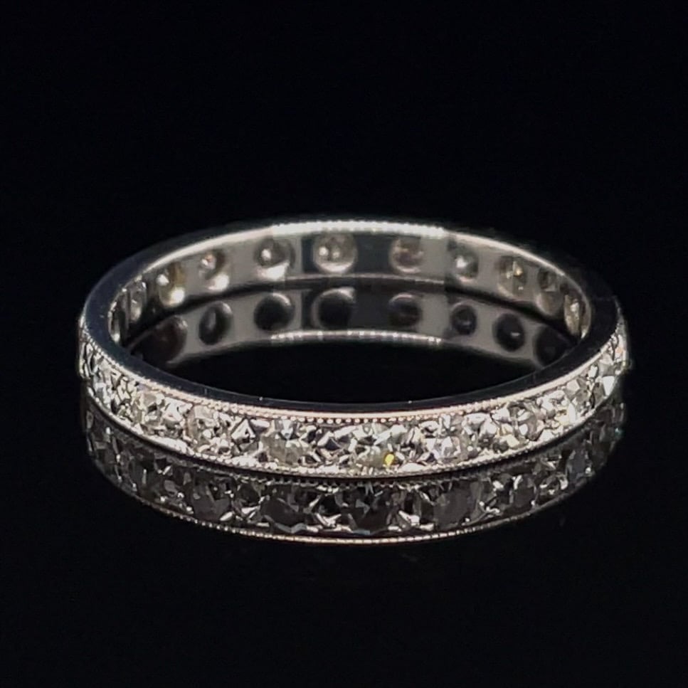 Double-row diamond eternity ring in silver metal on a black background, shimmering stones around the band.