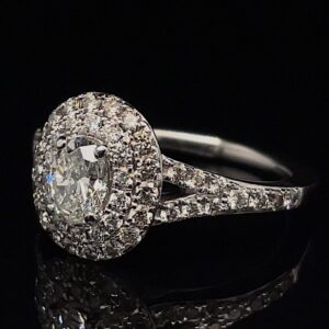 Engagement ring with a large oval-cut center diamond surrounded by a halo of pavé diamonds and a diamond-studded band in white metal.