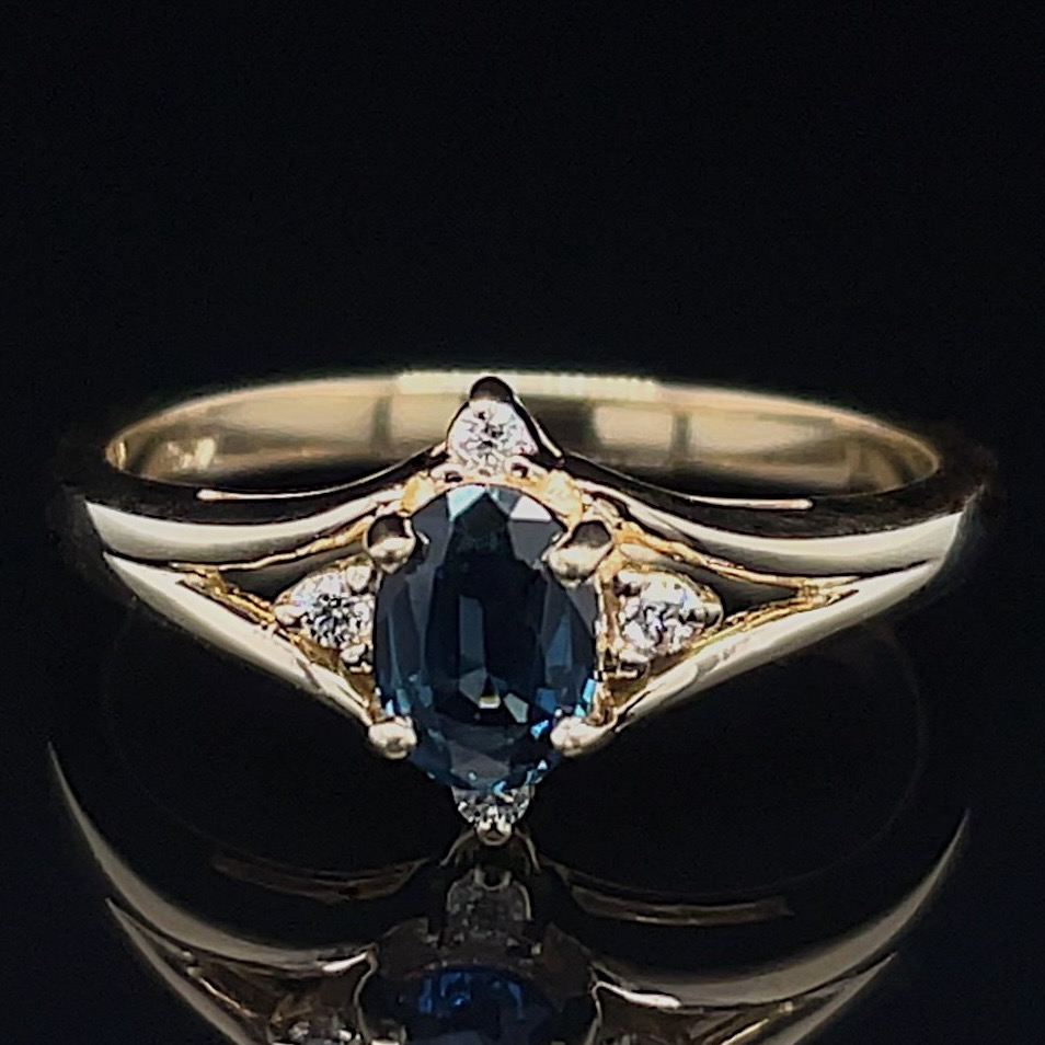 Gold ring with an oval blue gemstone and small surrounding diamonds on a dark background (prominent central sapphire).