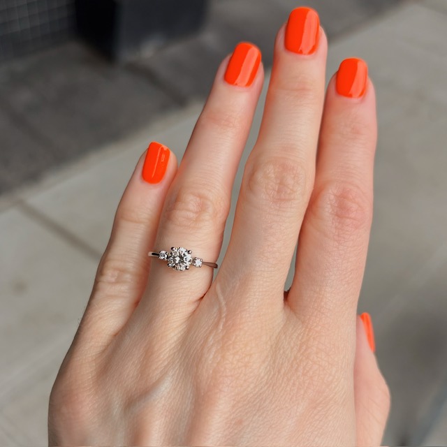 Left hand shows a diamond engagement ring on the ring finger with bright orange nail polish on all fingers