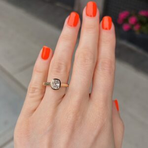 Hand with bright orange nails wearing a gold ring featuring a square-cut diamond on a finger.