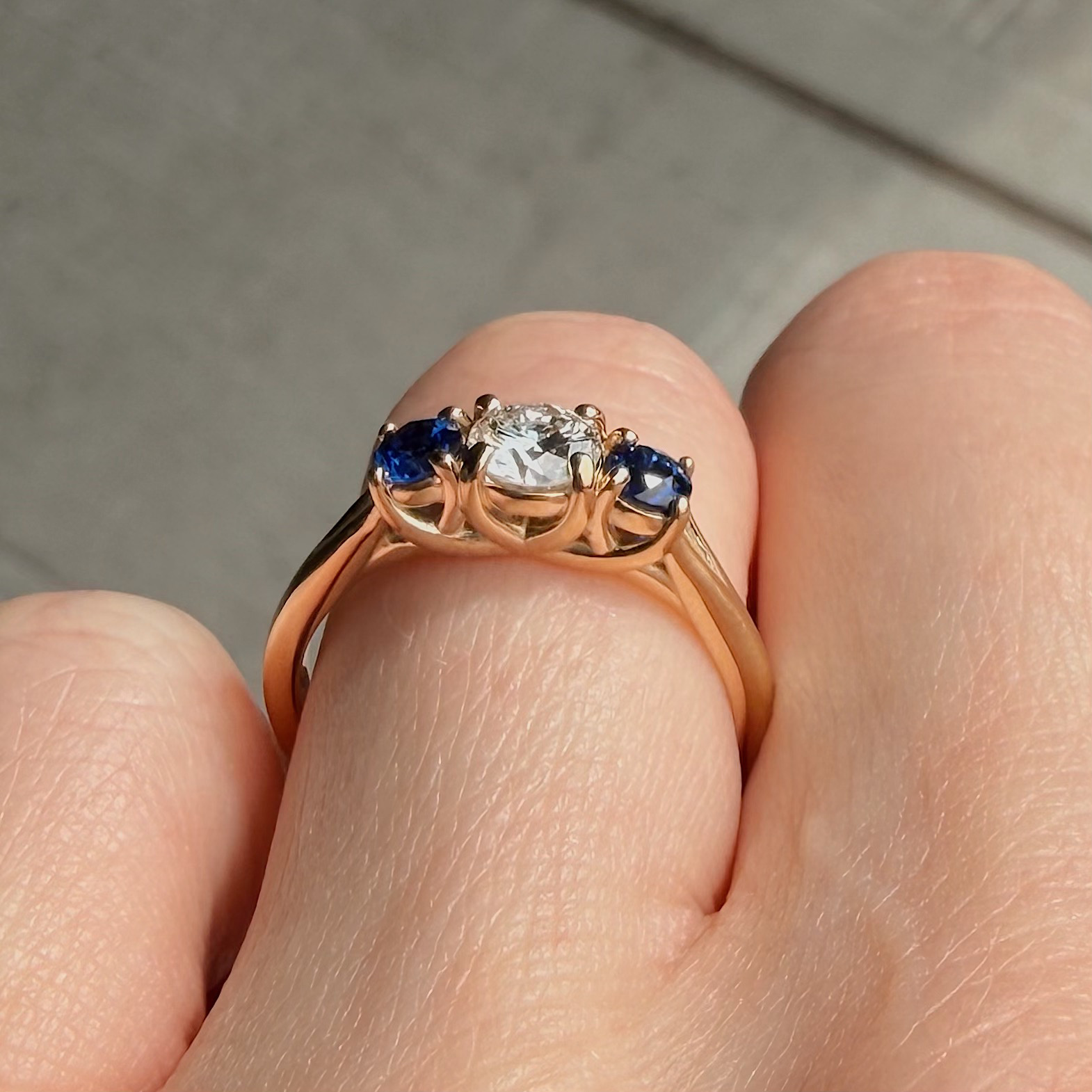 Close-up of a rose-gold ring with a central clear diamond flanked by blue sapphires on each side.