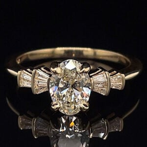 Engagement ring with a large oval diamond center and baguette side stones on a gold band against a black background