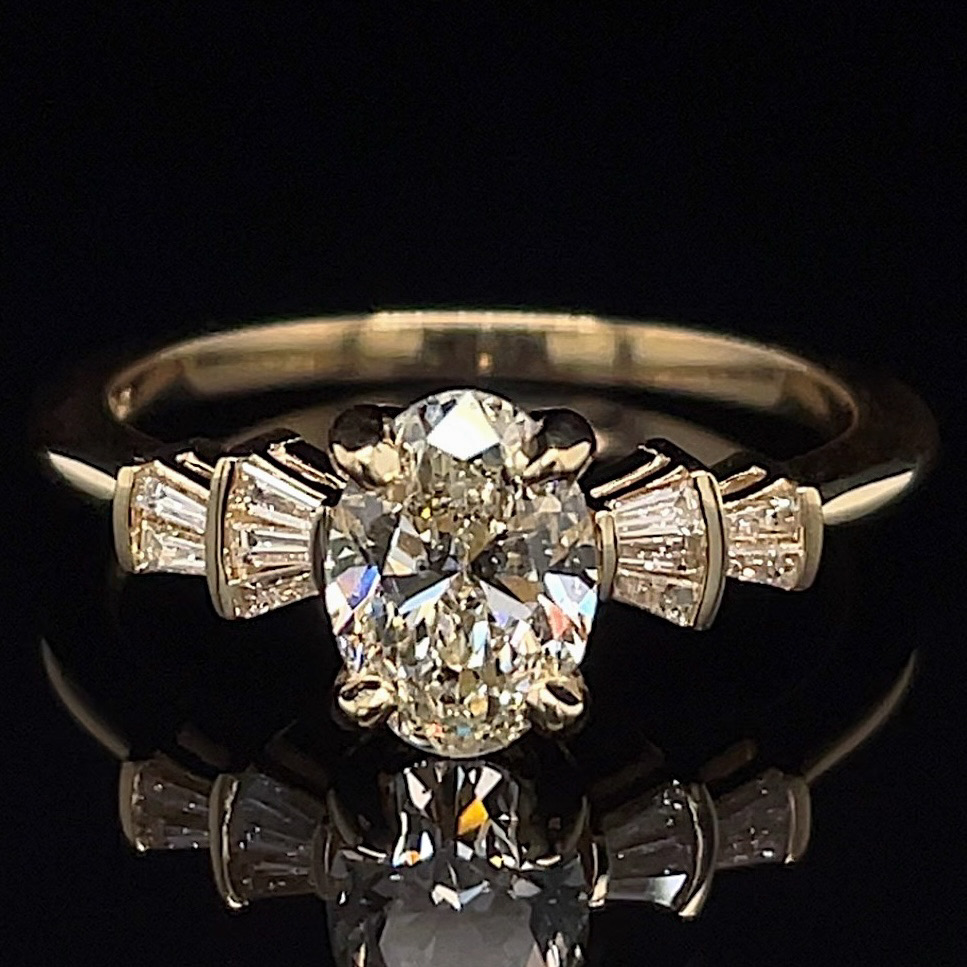 Engagement ring with a large oval diamond center and baguette side stones on a gold band against a black background