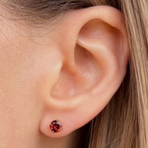Close-up of a left ear with a small round red gemstone stud earring in the earlobe.