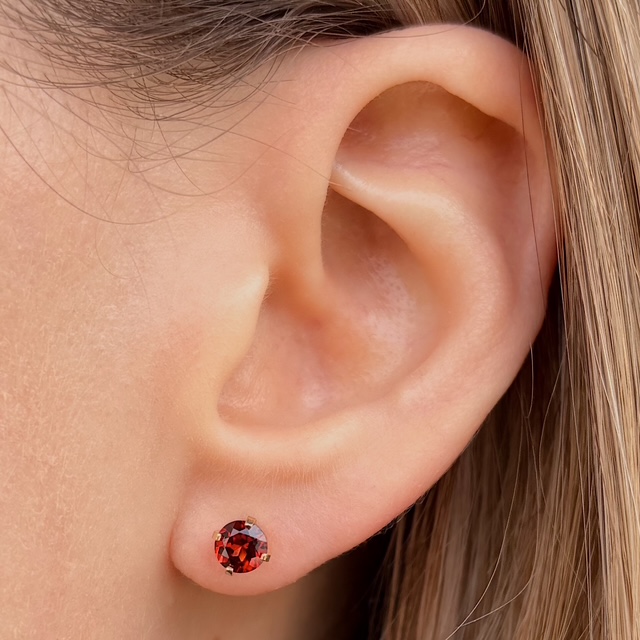 Close-up of a left ear with a small round red gemstone stud earring in the earlobe.