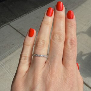 Close-up of a hand with glossy red manicure and a thin diamond ring on the ring finger.