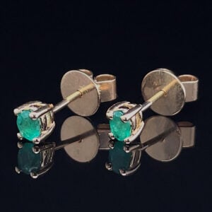 Pair of silver cufflinks with bright green gemstones on a reflective black surface.