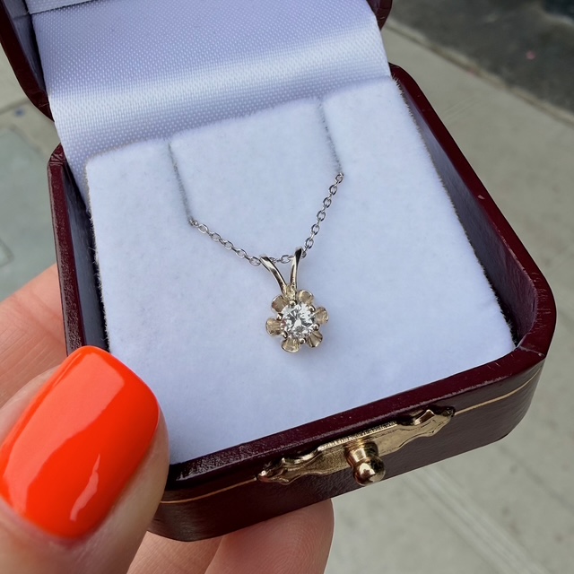 Delicate silver chain necklace with a six-petal flower pendant featuring a central gemstone, displayed in a white cushioned jewelry box inside a burgundy case.