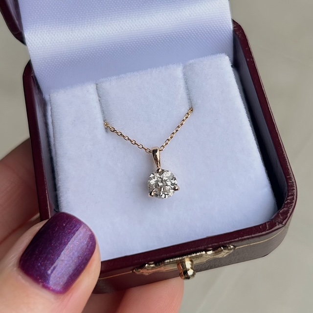 Gold chain necklace with a round diamond pendant in a white cushioned jewelry box.