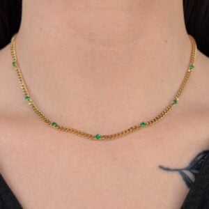 Gold chain necklace with evenly spaced green gemstones around a person’s neck.
