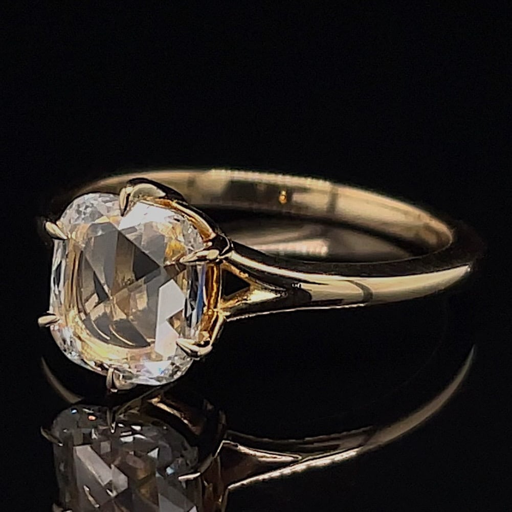 Gold engagement ring with a large oval-cut diamond on a black reflective surface