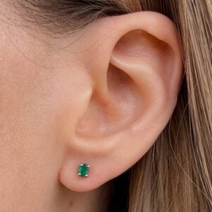 Close-up of a woman's left earlobe with a small square-cut emerald stud earring.