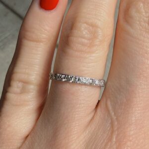 Close-up of a silver diamond eternity ring worn on the ring finger, with small stones all around the band