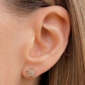 Close-up of a pierced earlobe wearing a small star-shaped diamond stud earring in gold.