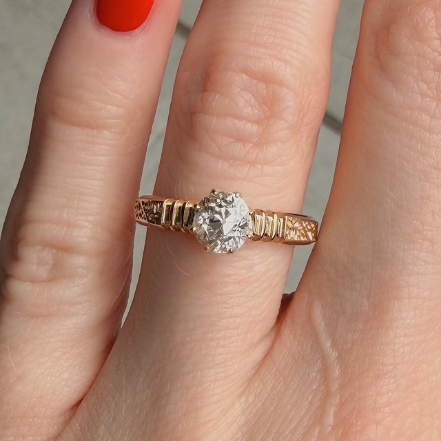 Rose gold engagement ring with a large round diamond on a finger, close-up.