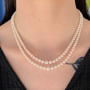 Two-layer pearl necklace resting on a person's neck over a black top, with a small chest tattoo visible.
