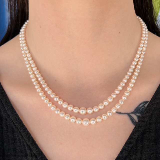 Two-layer pearl necklace resting on a person's neck over a black top, with a small chest tattoo visible.
