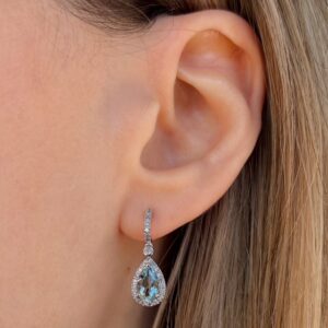 Teardrop diamond drop earring with a pavé halo worn on the earlobe.