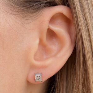 Close-up of an ear with a small square-cut diamond stud earring in a silver setting on the earlobe.