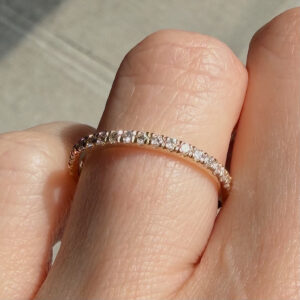 Close-up of a diamond eternity ring worn on a finger, with small sparkling stones around the band.