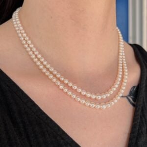 Two strands of white pearl necklaces draped around a person's neck against a black top.